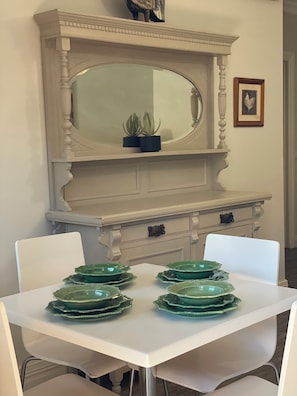 A dining area with a white table set for four, a white chair, a white cabinet with a mirror, and a framed picture on the wall. - CocknBull Boutique Hotel (Echuca)