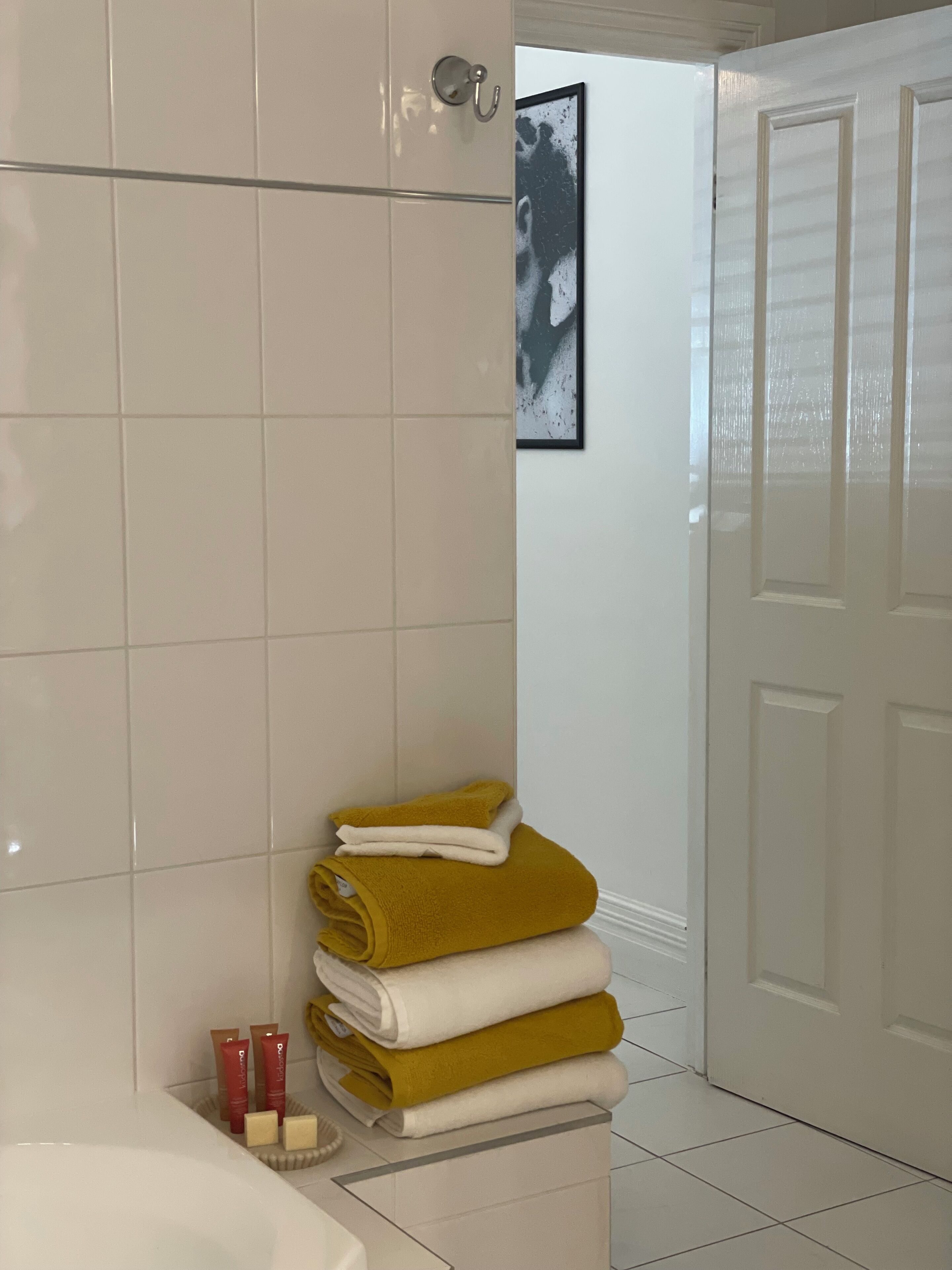 Une salle de bain carrelée de blanc, avec une baignoire blanche et une pile d’serviettes.