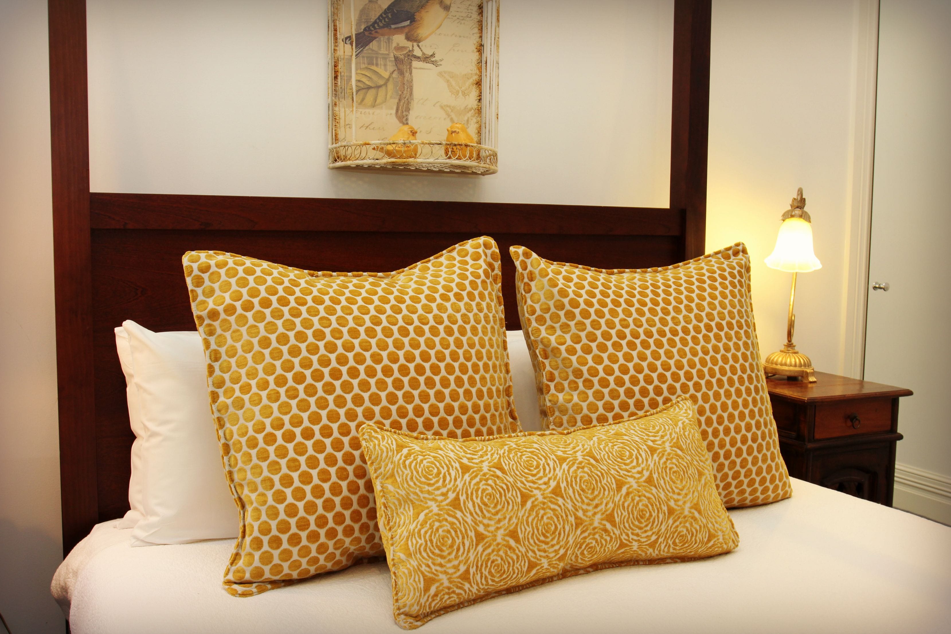 Cama bem arrumada com cabeceira de madeira, luminária de cabeceira e uma obra de arte emoldurada acima da cama.