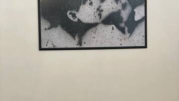 A framed artwork of a couple kissing on a white wall above a beige sofa with two cushions.