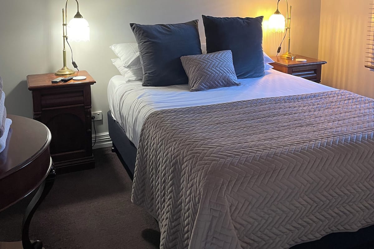 Un dormitorio con cama, dos mesitas de noche con lámparas, ventilador de techo y tres cuadros en la pared.