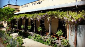 A hotel with a 'Boutique' sign, outdoor seating, and a garden area with purple flowers. - CocknBull Boutique Hotel (Echuca)