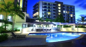 A modern hotel with a swimming pool, outdoor seating, and palm trees.