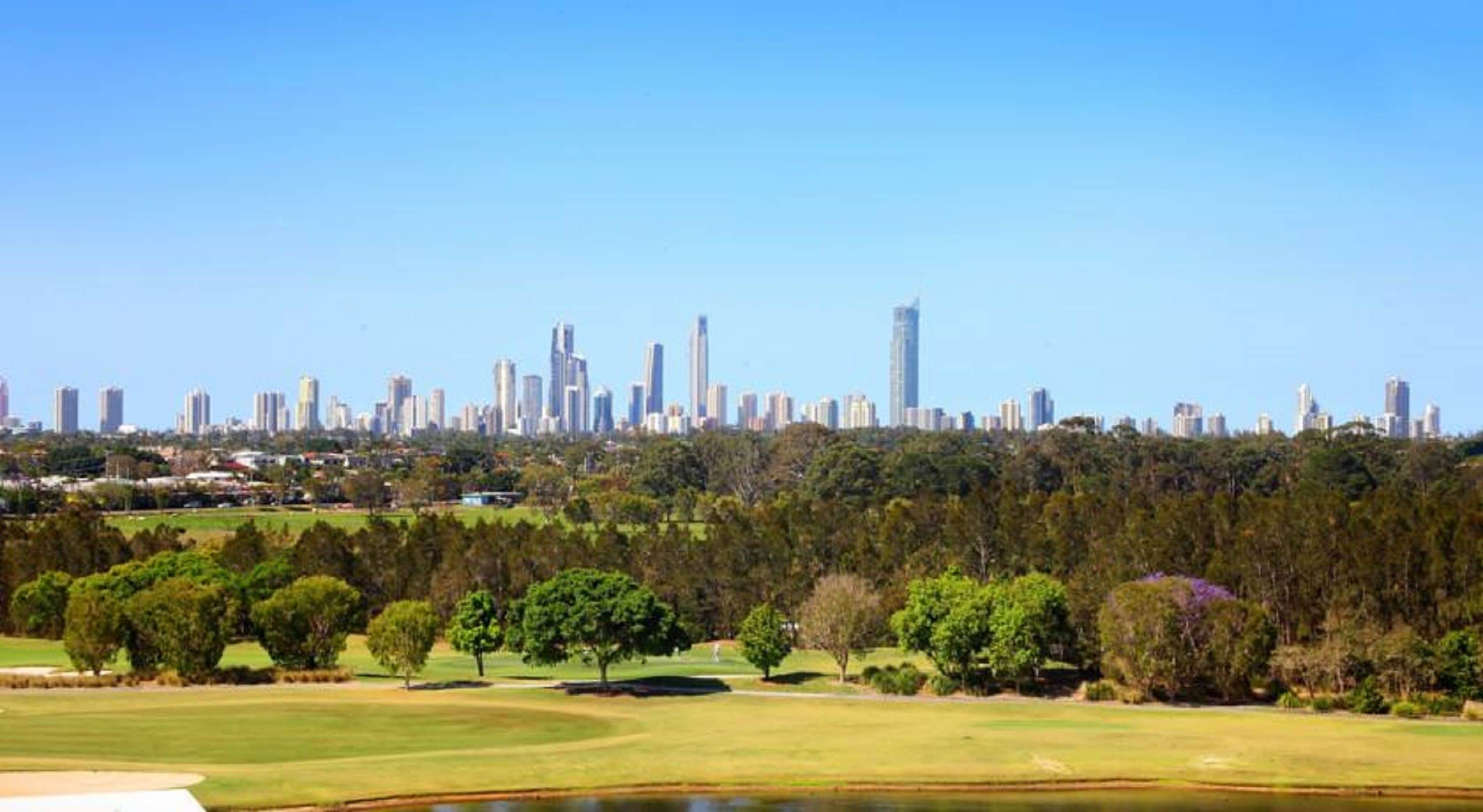 Un horizonte urbano con edificios altos modernos, un campo de golf con árboles y un estanque, y un cielo azul despejado.