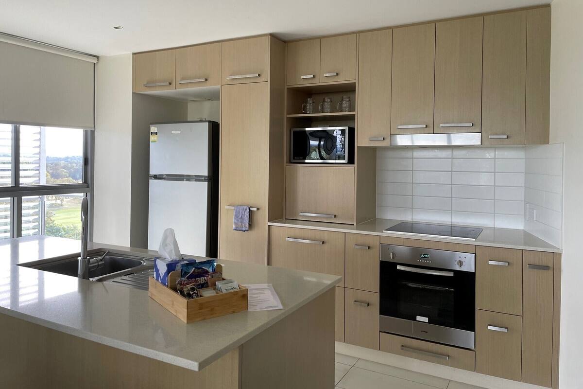 A modern kitchen with wooden cabinets, a stainless steel refrigerator, a microwave, and an oven.