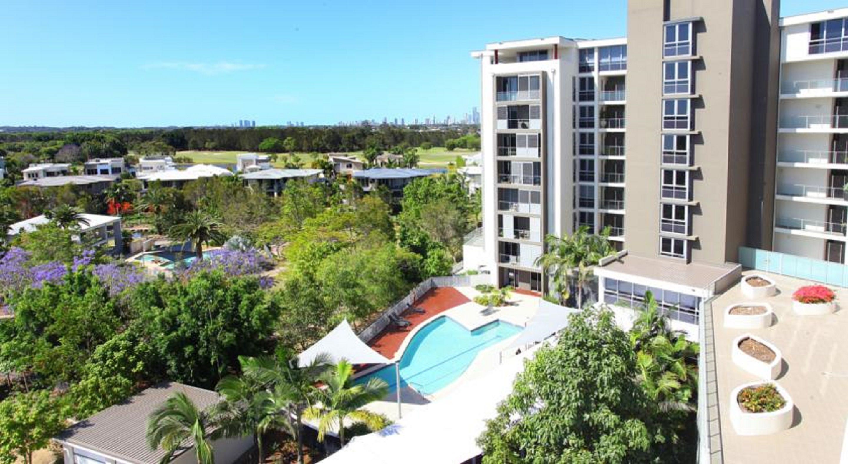 A high-rise hotel with multiple balconies, a swimming pool, and lush greenery surrounding the property.