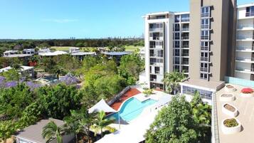 A high-rise hotel with multiple balconies, a swimming pool, and lush greenery surrounding the property.