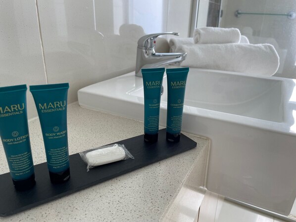 A bathroom with a white sink, two MARU body lotion tubes, and a bar of soap on a black tray.