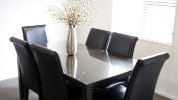A conference room with a dark wooden table, six black leather chairs, a vase with white flowers, and an air conditioning unit on the wall.