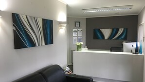 A reception area with a white desk, black leather couch, and abstract wall art. - Camelot on Ulster (Hamilton)