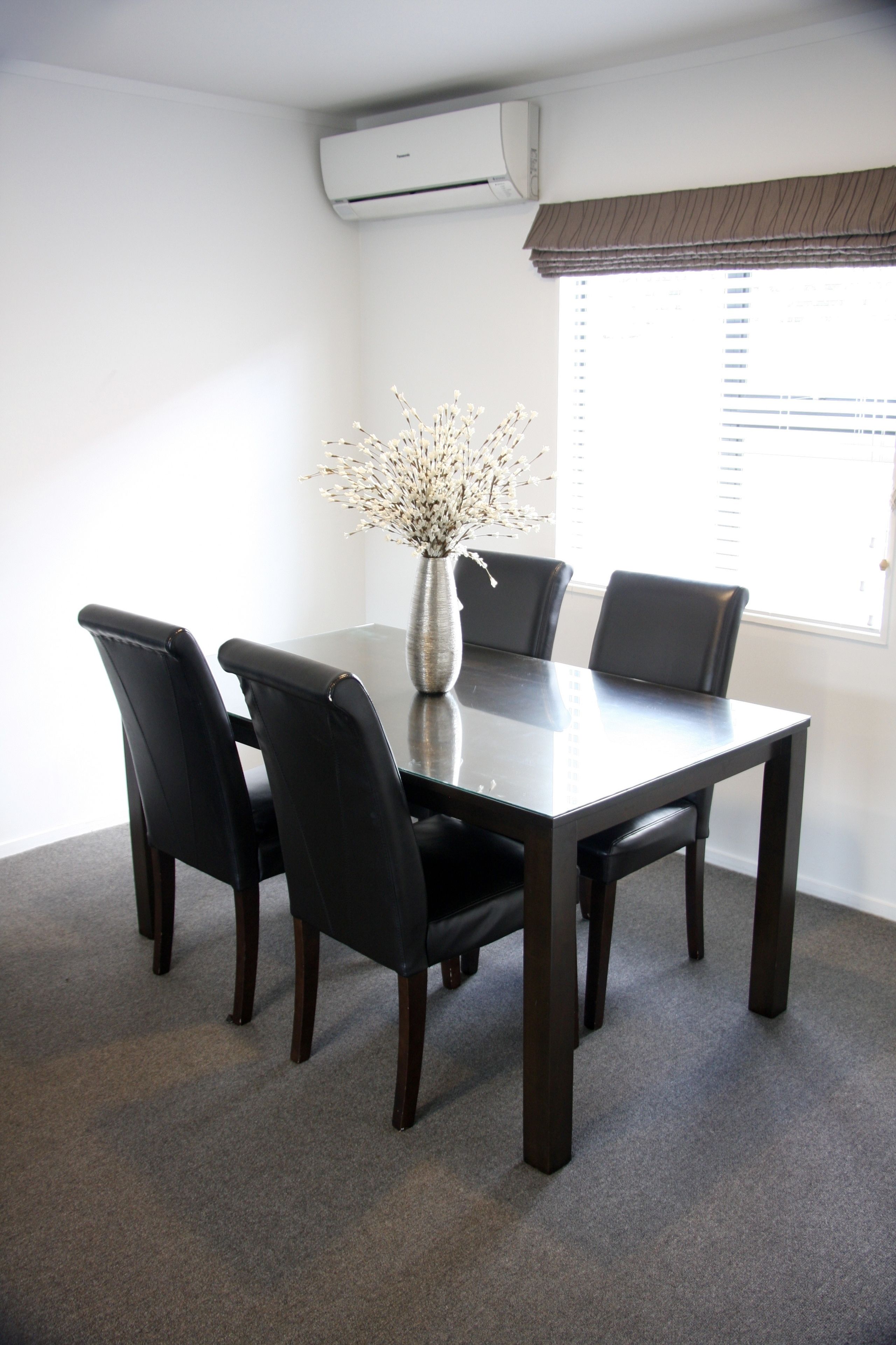A conference room with a dark wooden table, four black chairs, and a vase with white flowers.