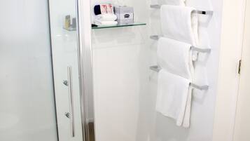 A modern bathroom with a glass shower enclosure, a wooden floor, and a towel rack with multiple white towels.