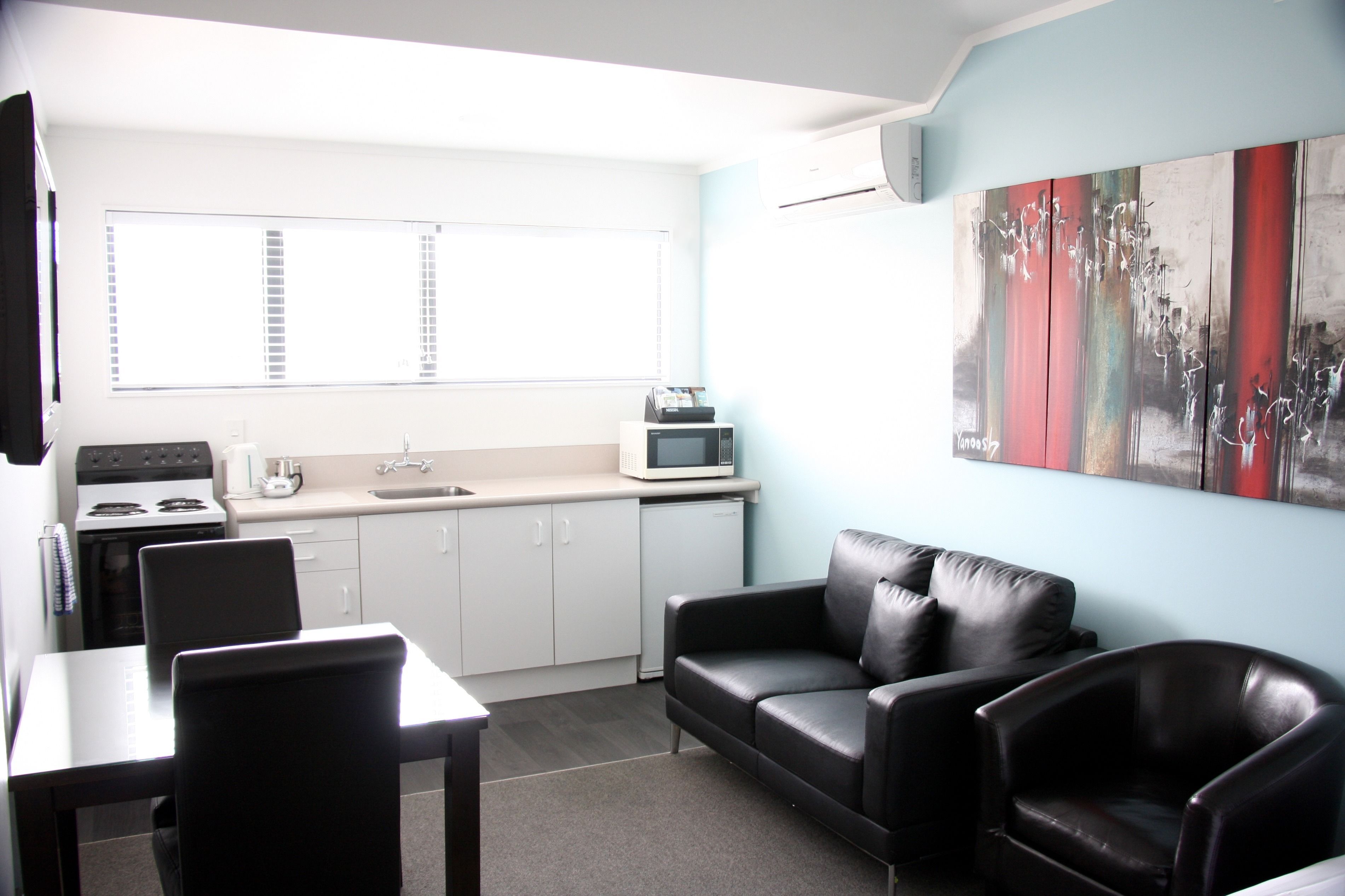 Un espacio habitable compacto con kitchenette, comedor y zona de estar con sofá de cuero negro.