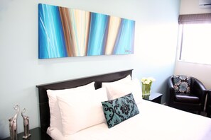 Quarto de hotel com uma cama, um travesseiro decorativo, um vaso com flores e uma cadeira.