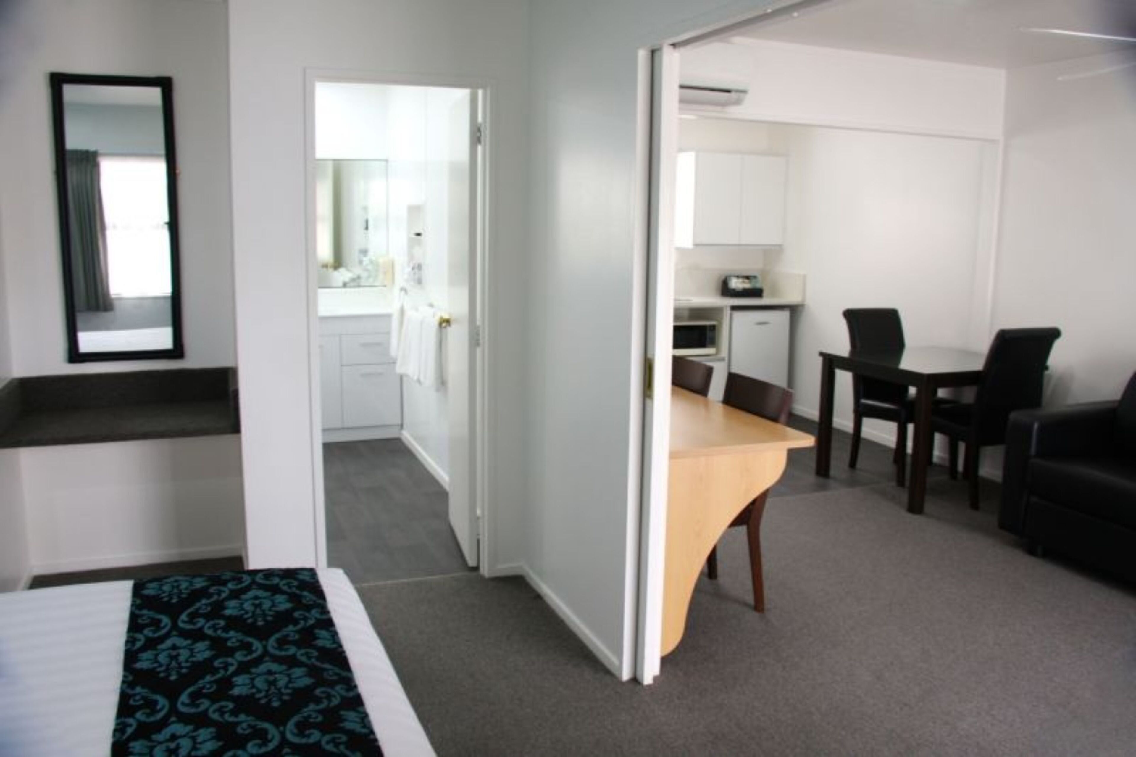Habitación de hotel con cama, escritorio, silla, kitchenette pequeña y espejo.