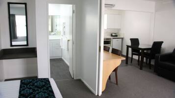 Habitación de hotel con cama, escritorio, silla, kitchenette pequeña y espejo.