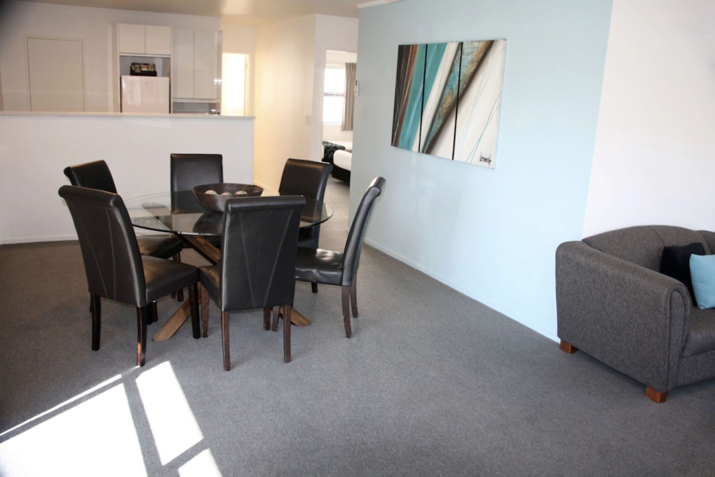 A modern kitchen with white cabinets, a dining table with chairs, and a grey sofa.