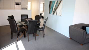 A modern kitchen with white cabinets, a dining table with chairs, and a grey sofa.