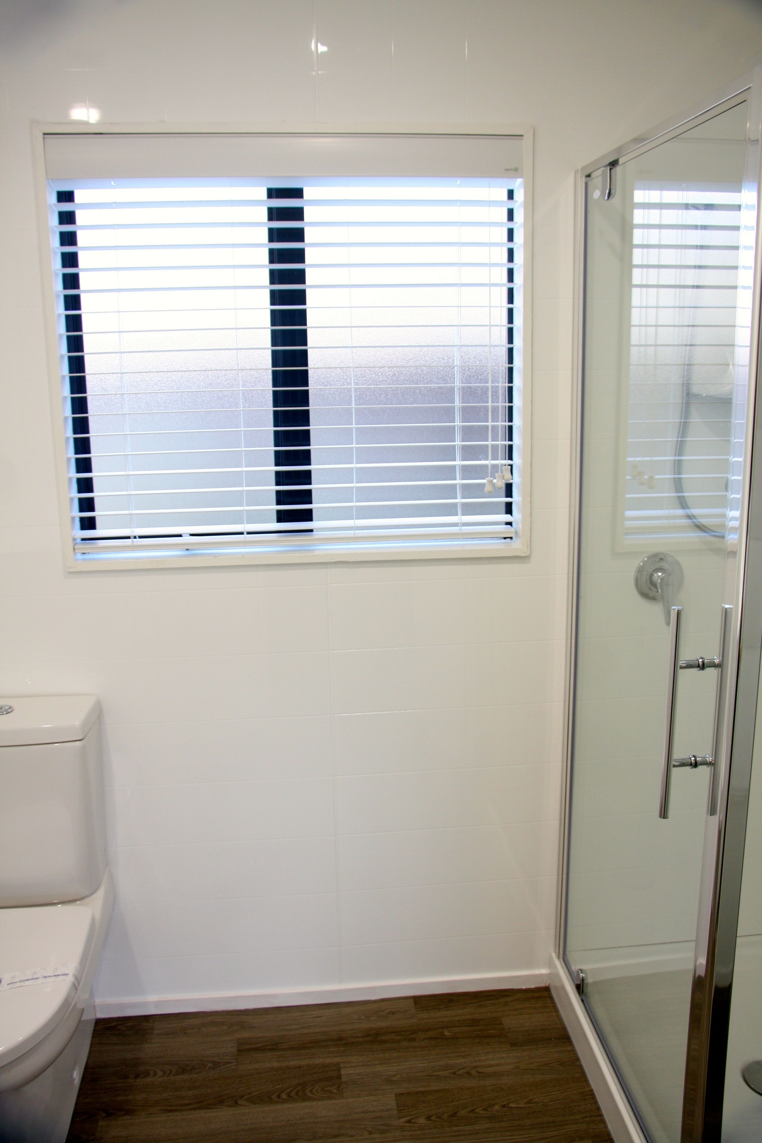 A bathroom with a toilet, a window with blinds, and a glass shower enclosure.