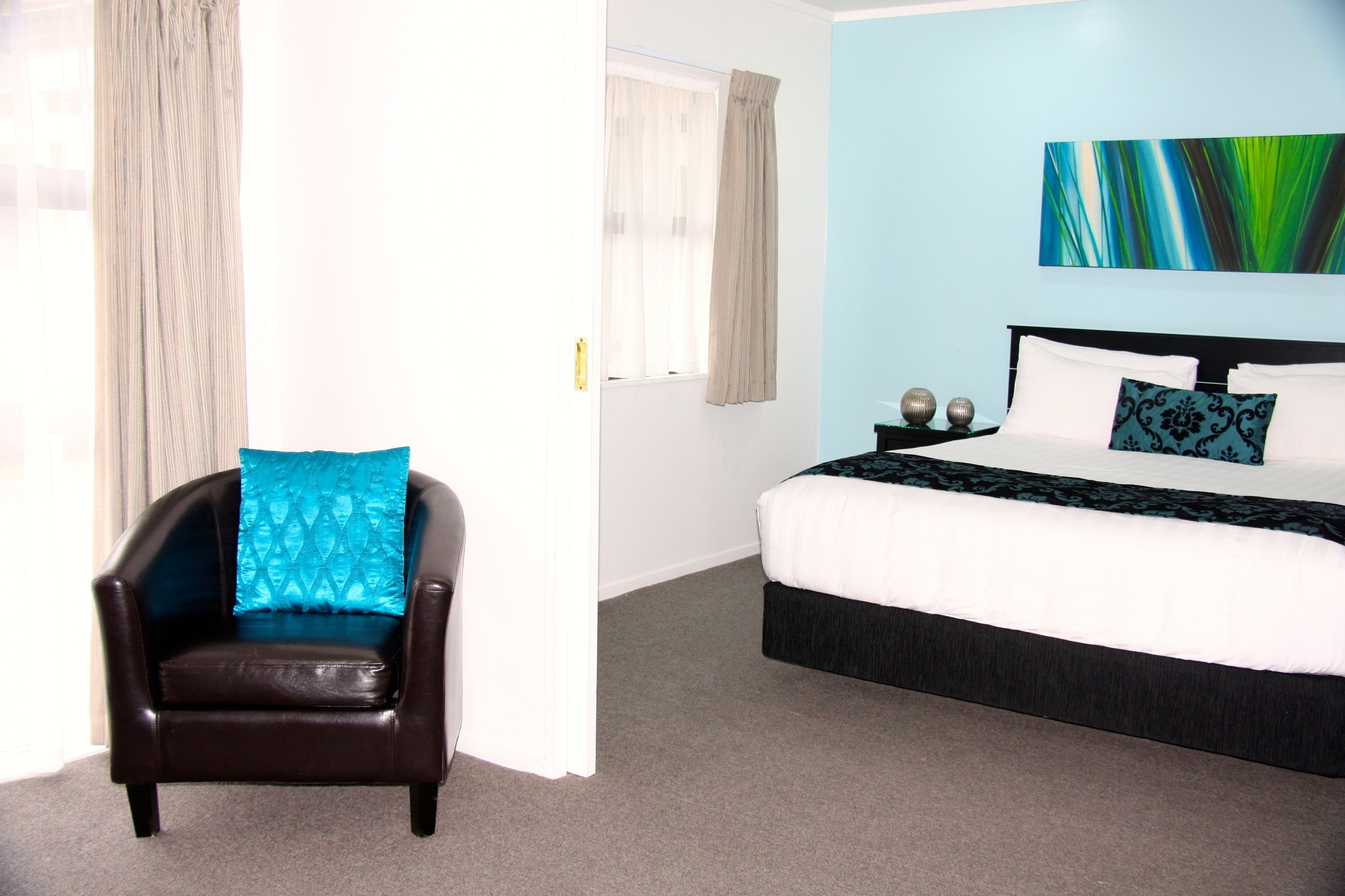 A hotel room with a bed, a chair, and a painting on the wall.