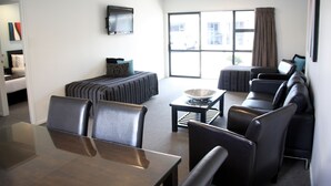 A modern living room with a dining area, a sofa set, a TV mounted on the wall, and a large window with curtains. - Camelot on Ulster (Hamilton)