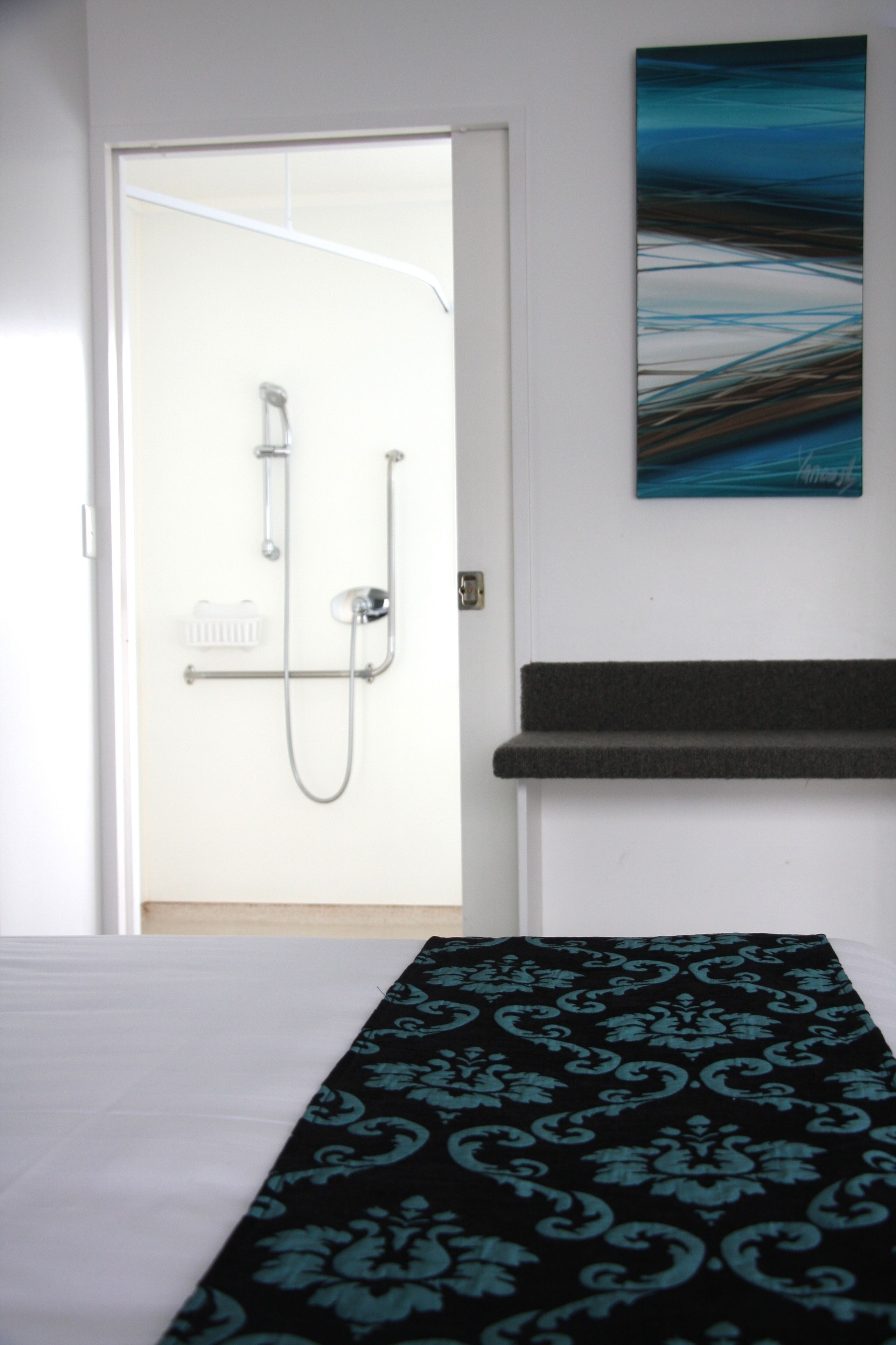A hotel room with a bed, a shower, and a painting on the wall.