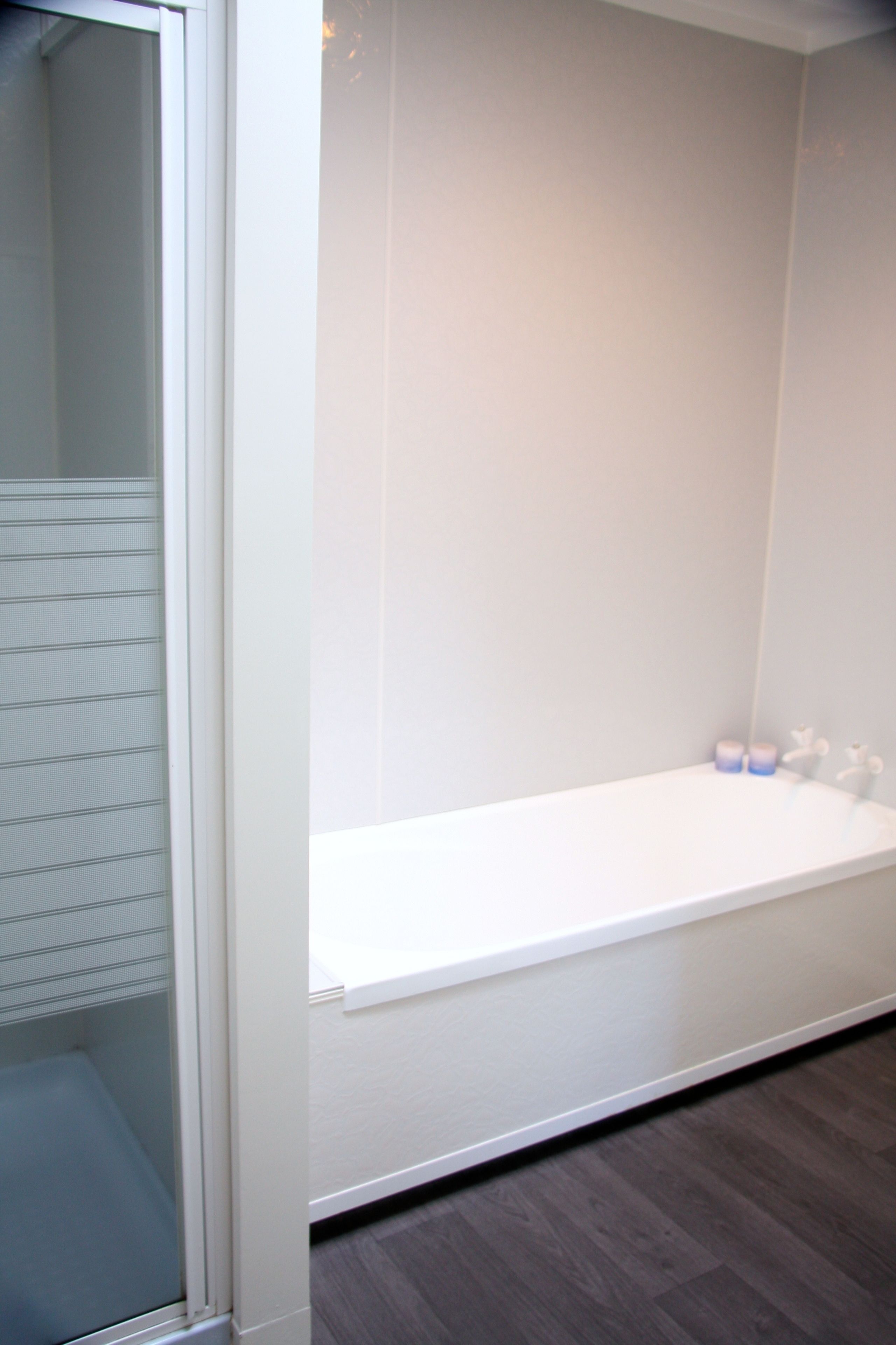 A modern bathroom with a glass shower enclosure, a white bathtub, and a wooden floor.