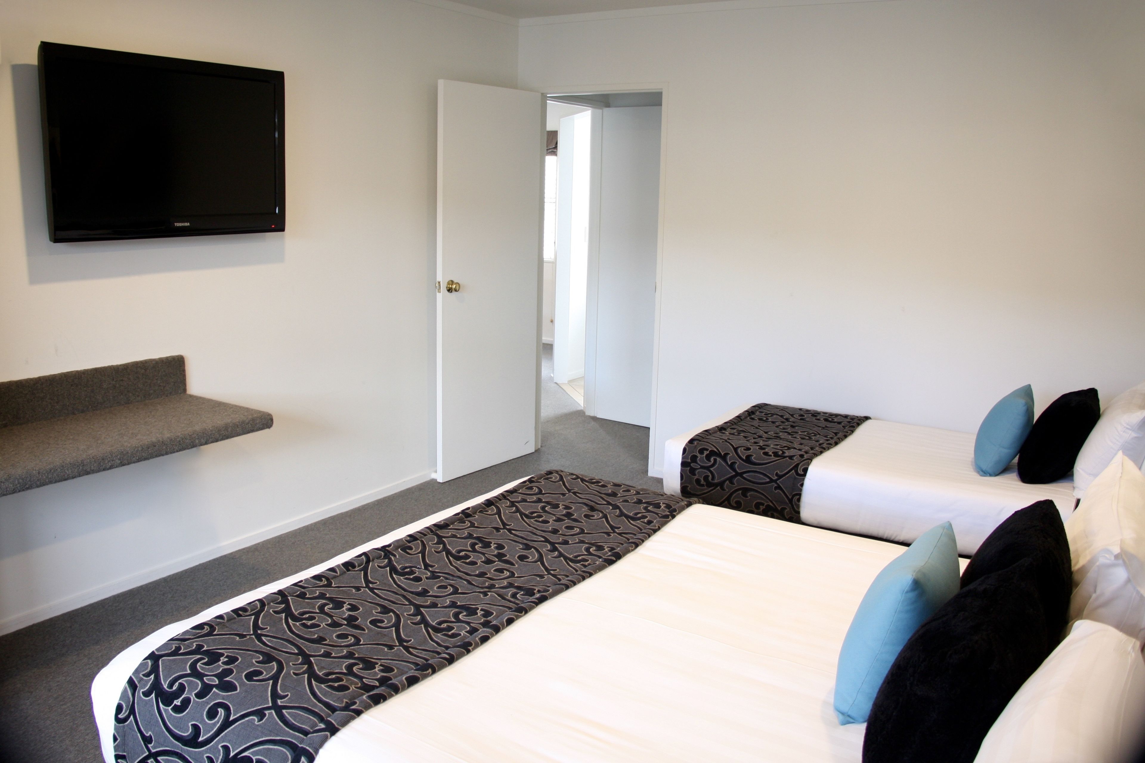 A hotel room with a flat-screen TV mounted on the wall, a staircase, and two beds with patterned bedspreads and pillows.