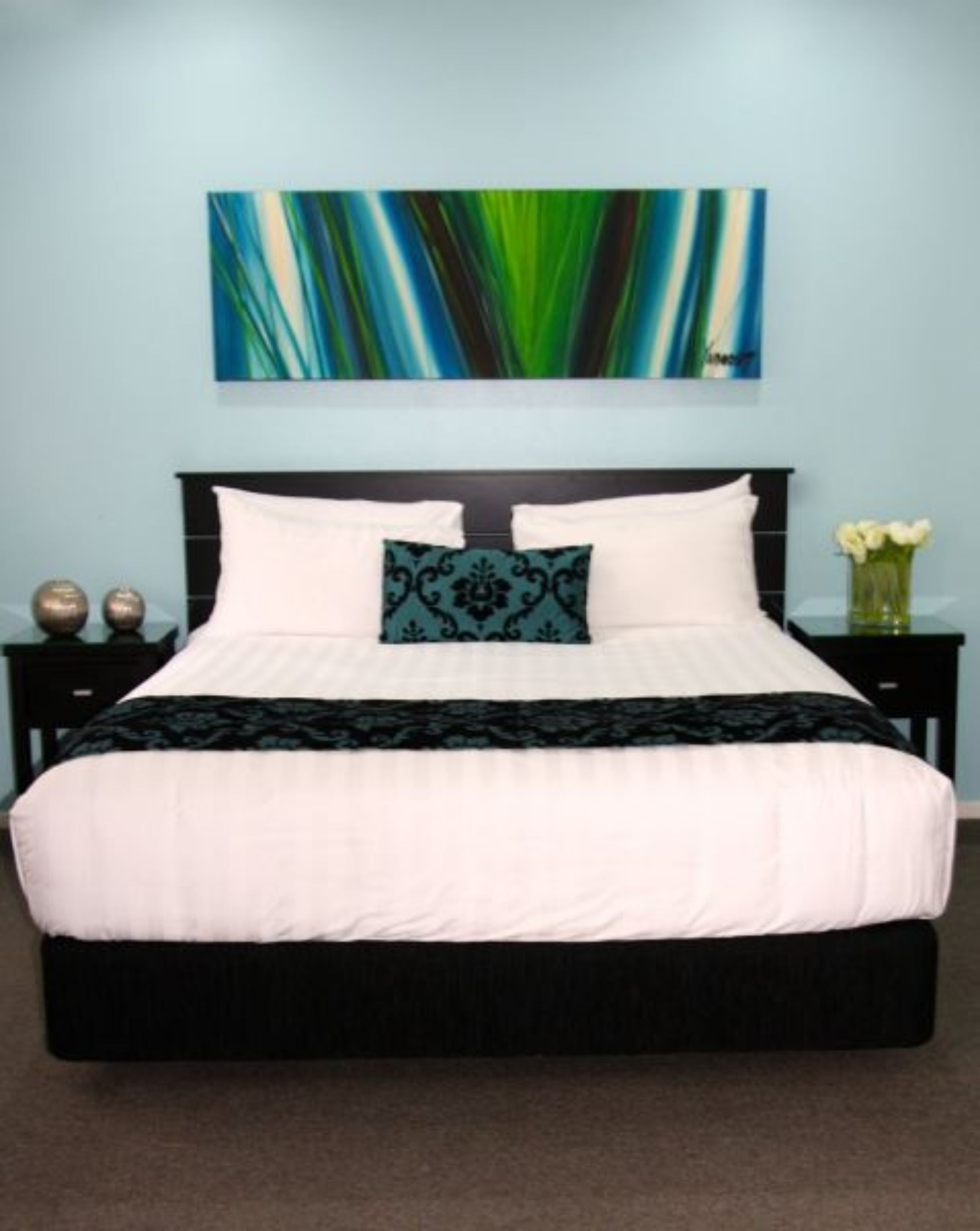 A bed with white and black bedding, a decorative pillow, and a painting on the wall.