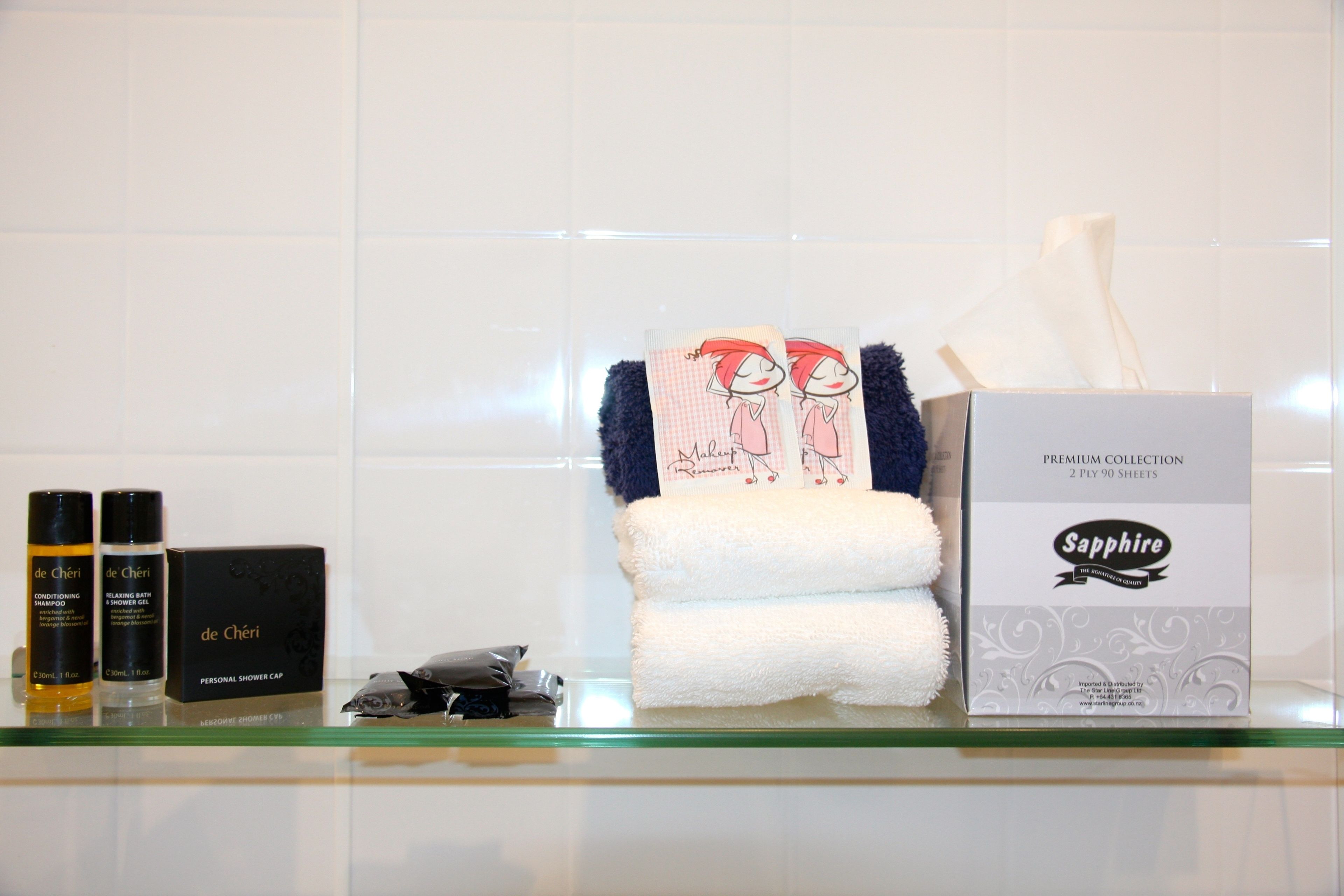 A bathroom shelf with personal care items including a box of 'Sapphire' tissues, a 'de Chéri' personal shower cap, and two 'de Chéri' hair care products.