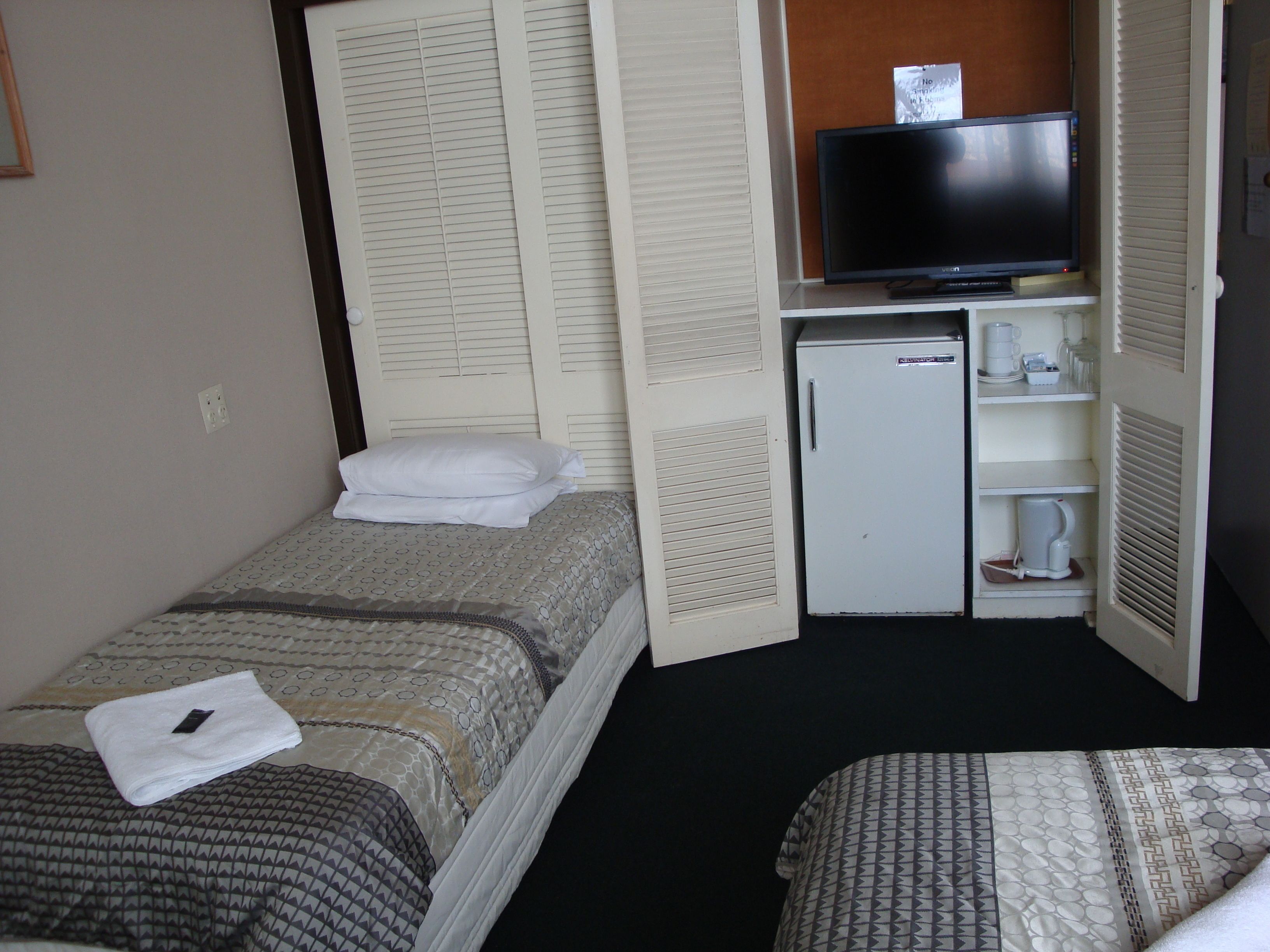 A compact hotel room with a bed, a television, a mini-fridge, and a coffee maker.