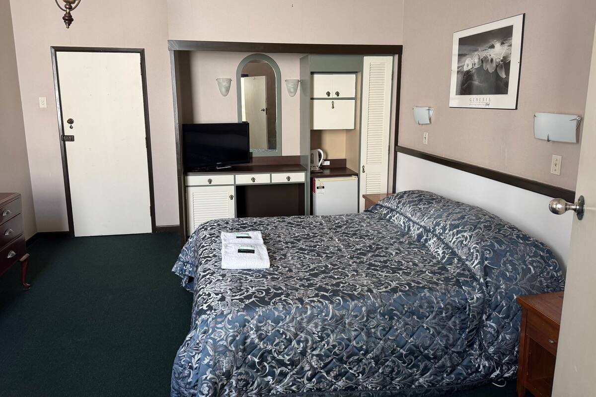 A hotel room with a bed, a desk, a television, a mirror, and a wardrobe.