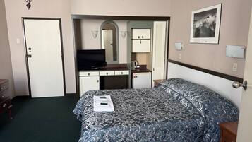 Ett hotellrum med en säng, ett skrivbord, en tv, en spegel och en garderob.