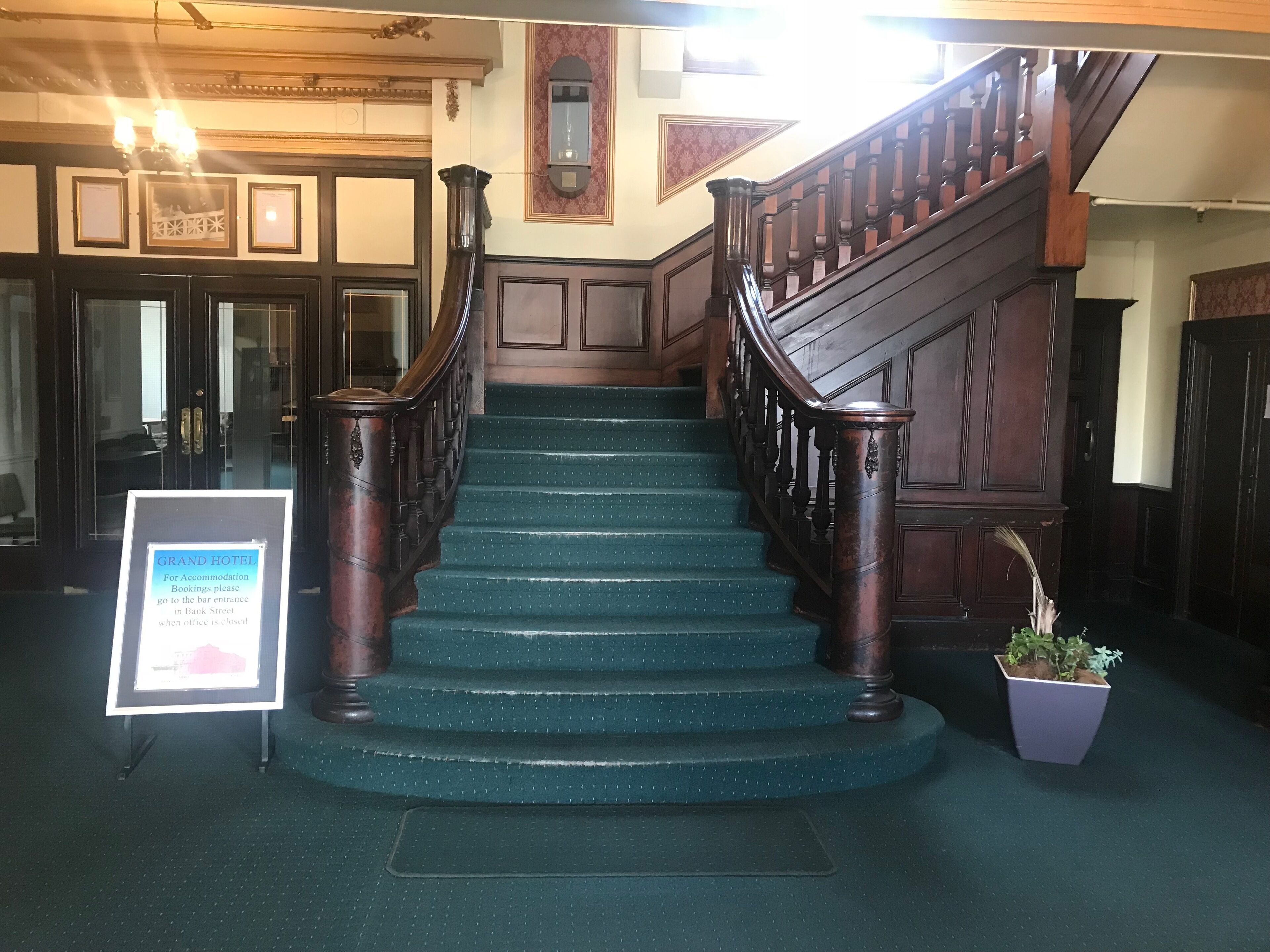 A grand hotel staircase with dark wooden railings and green carpeted steps.