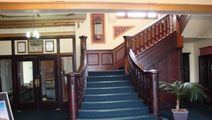 A grand staircase with wooden railings and blue carpeted steps leading to an upper floor. - Grand Hotel, Whangarei (Whangarei)