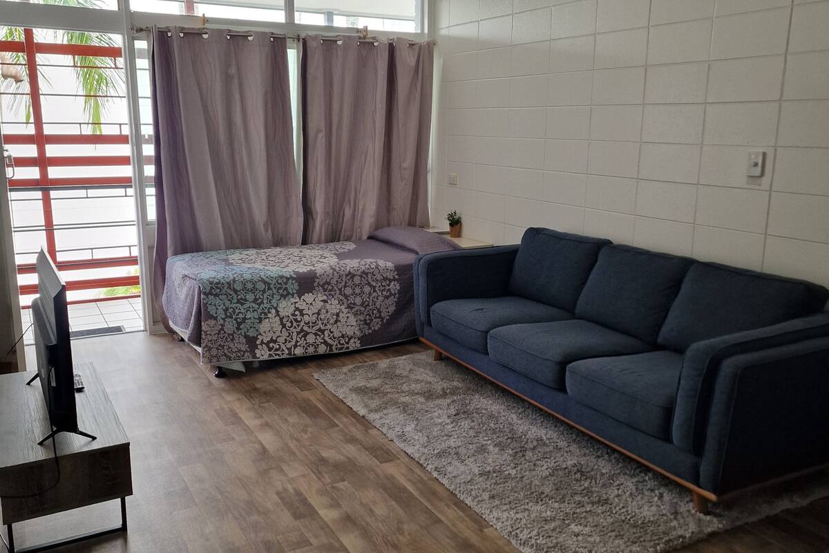 Un salon avec un canapé bleu foncé, un lit à motifs, une table basse en bois et un ventilateur de plafond.