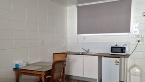 A compact kitchen with white cabinets, a microwave, a small refrigerator, and a dining area with a wooden table and chair. - A1 Inn the City (Cairns)