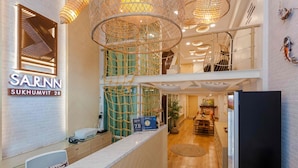 A hotel reception area with a modern design, including a reception desk, a digital display, and a staircase leading to an upper level. - Sarnn Sukhumvit 28 (Bangkok)