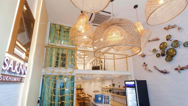 A modern hotel lobby with a high ceiling, netted pendant lights, a reception desk, and a view of the dining area. - Sarnn Sukhumvit 28 (Bangkok)