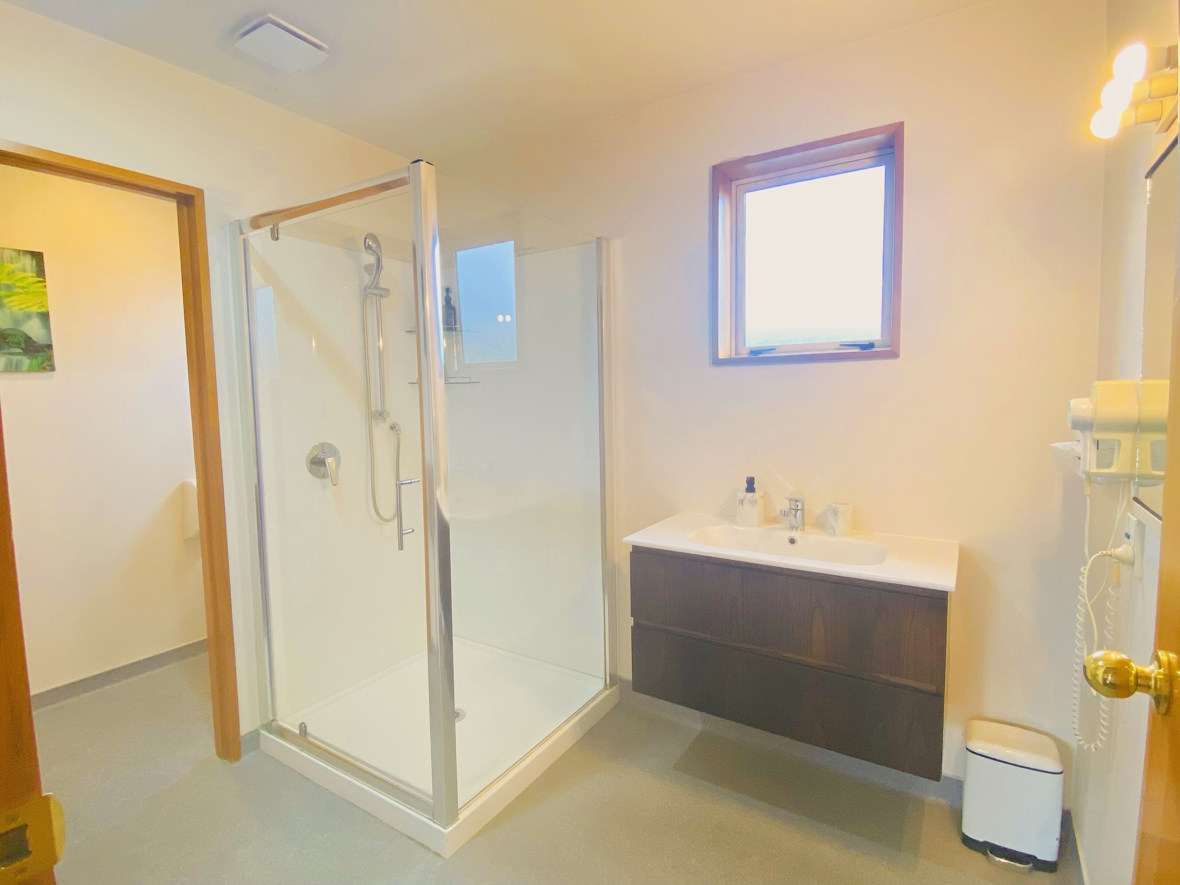 A bathroom with a glass shower enclosure, a sink with a mirror, and a small window.
