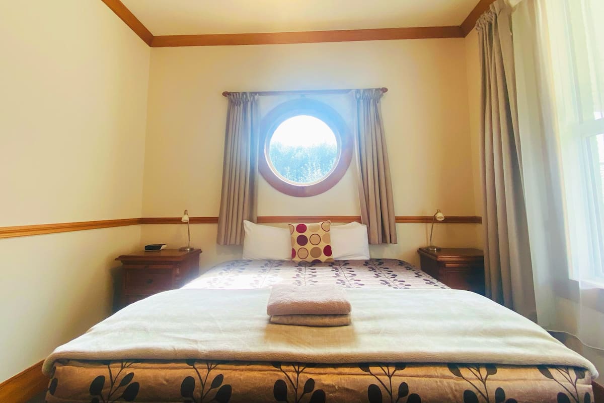 A hotel room with a large bed, a round window, and a view of the outdoors.
