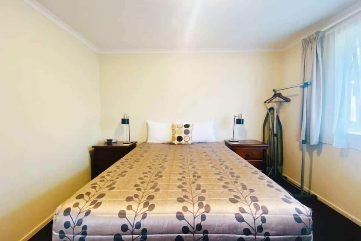 A hotel room with a bed, two bedside tables, a hanging coat rack, and a window with curtains.