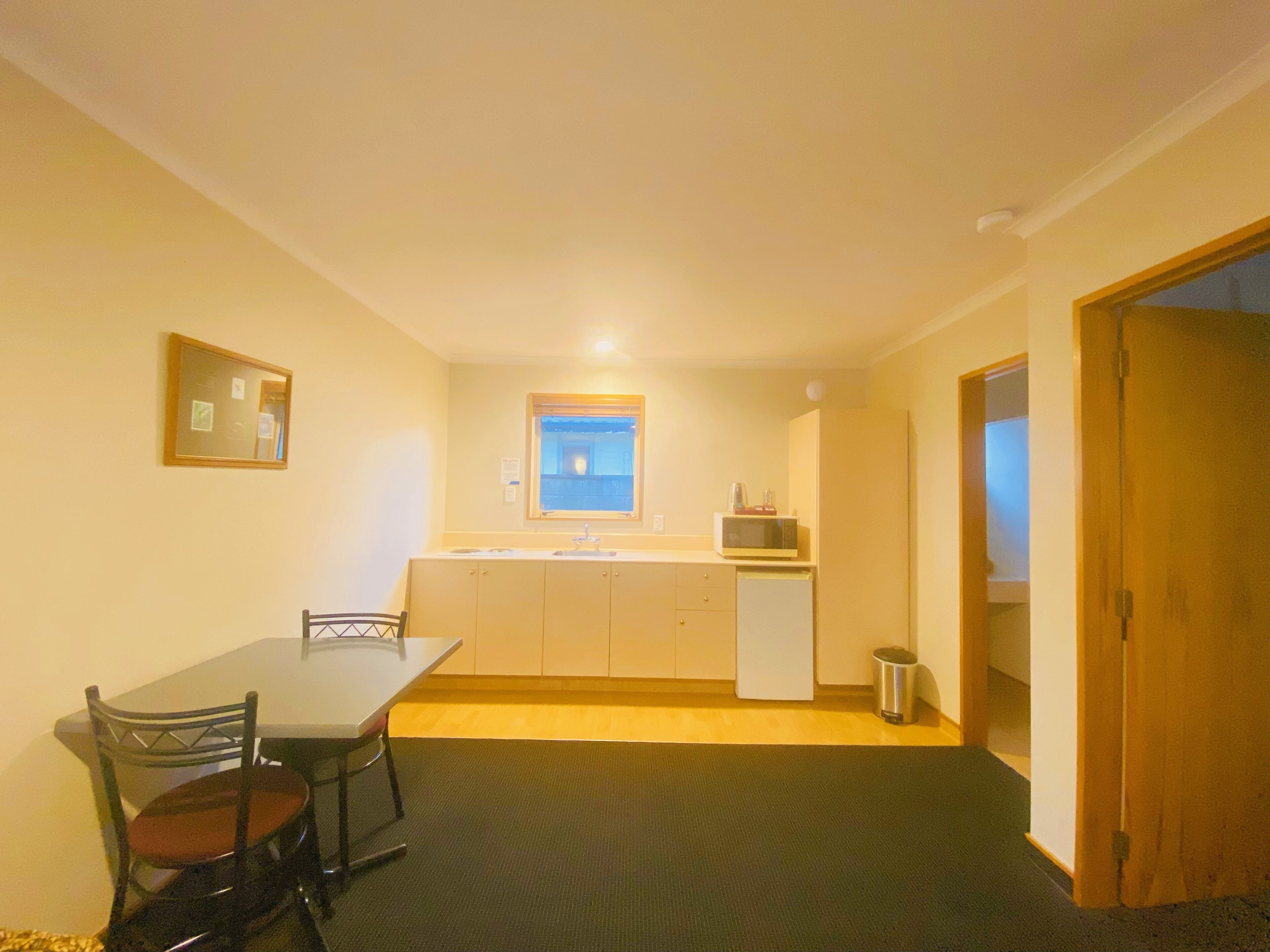 A compact kitchen with a dining table and chairs, a microwave, and a small window.