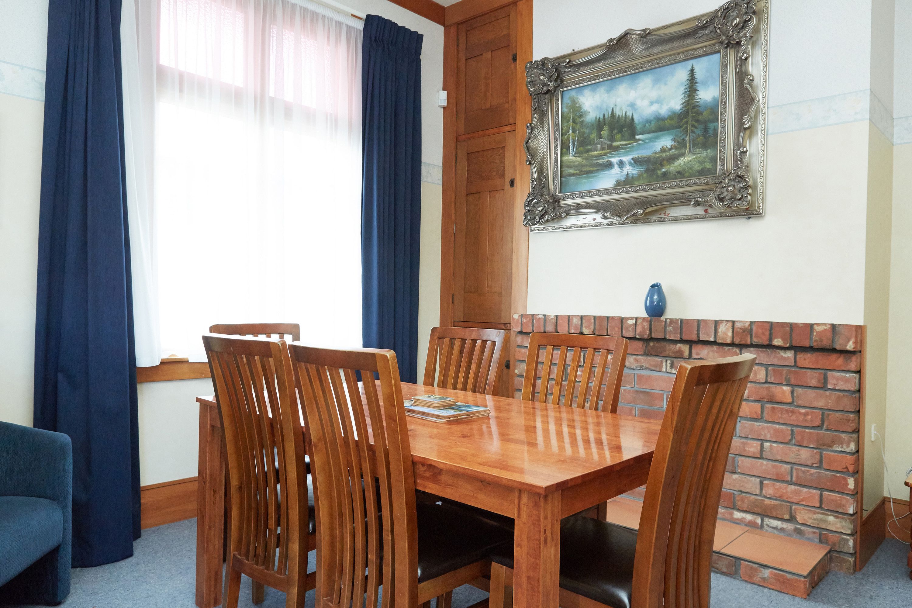 A dining area with a wooden table and chairs, a brick fireplace, and a framed painting on the wall.