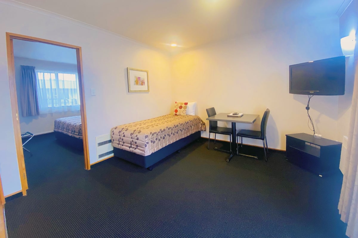 A hotel room with a bed, desk, chair, television, and a picture on the wall.