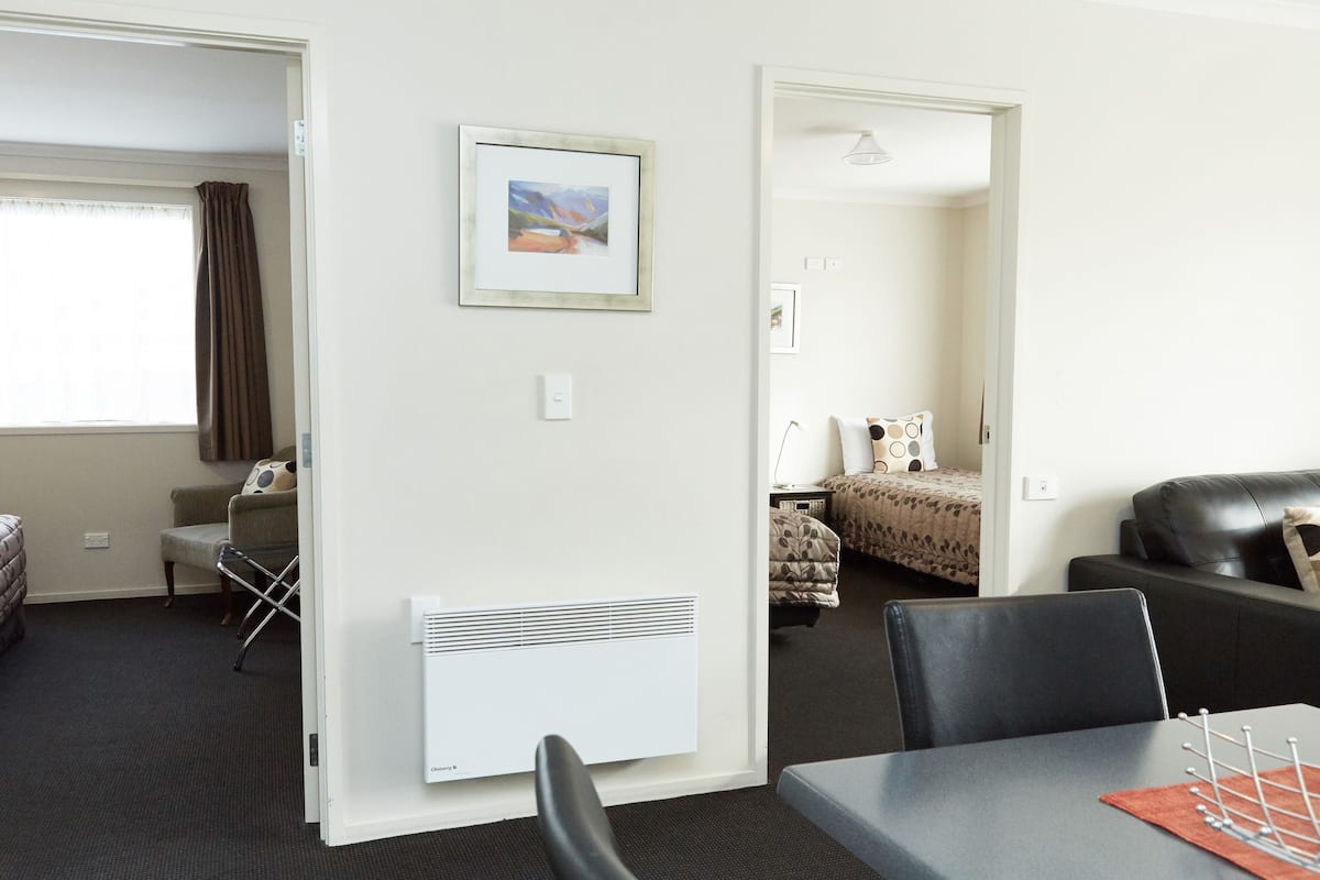 A hotel room with a dining area, a bed with a patterned bedspread, a black leather sofa, and a framed picture on the wall.