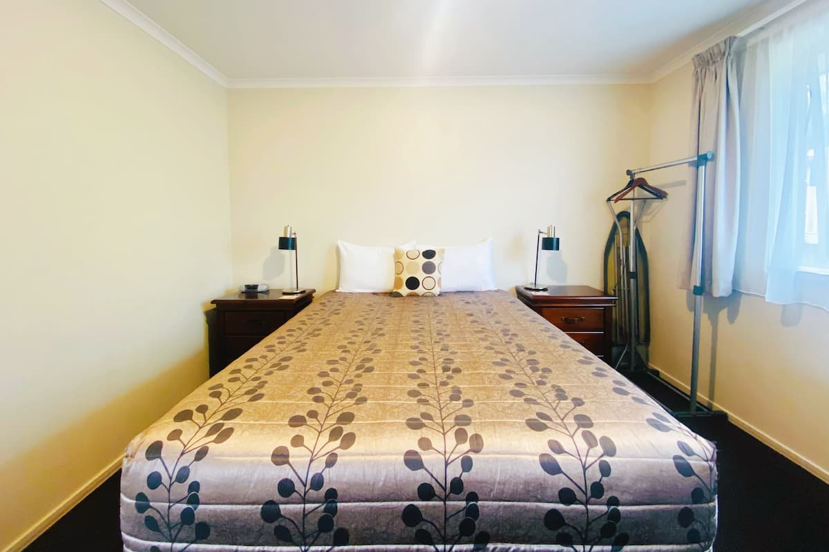 A hotel room with a bed, two bedside tables, a hanging clothes rack, and a window with curtains.