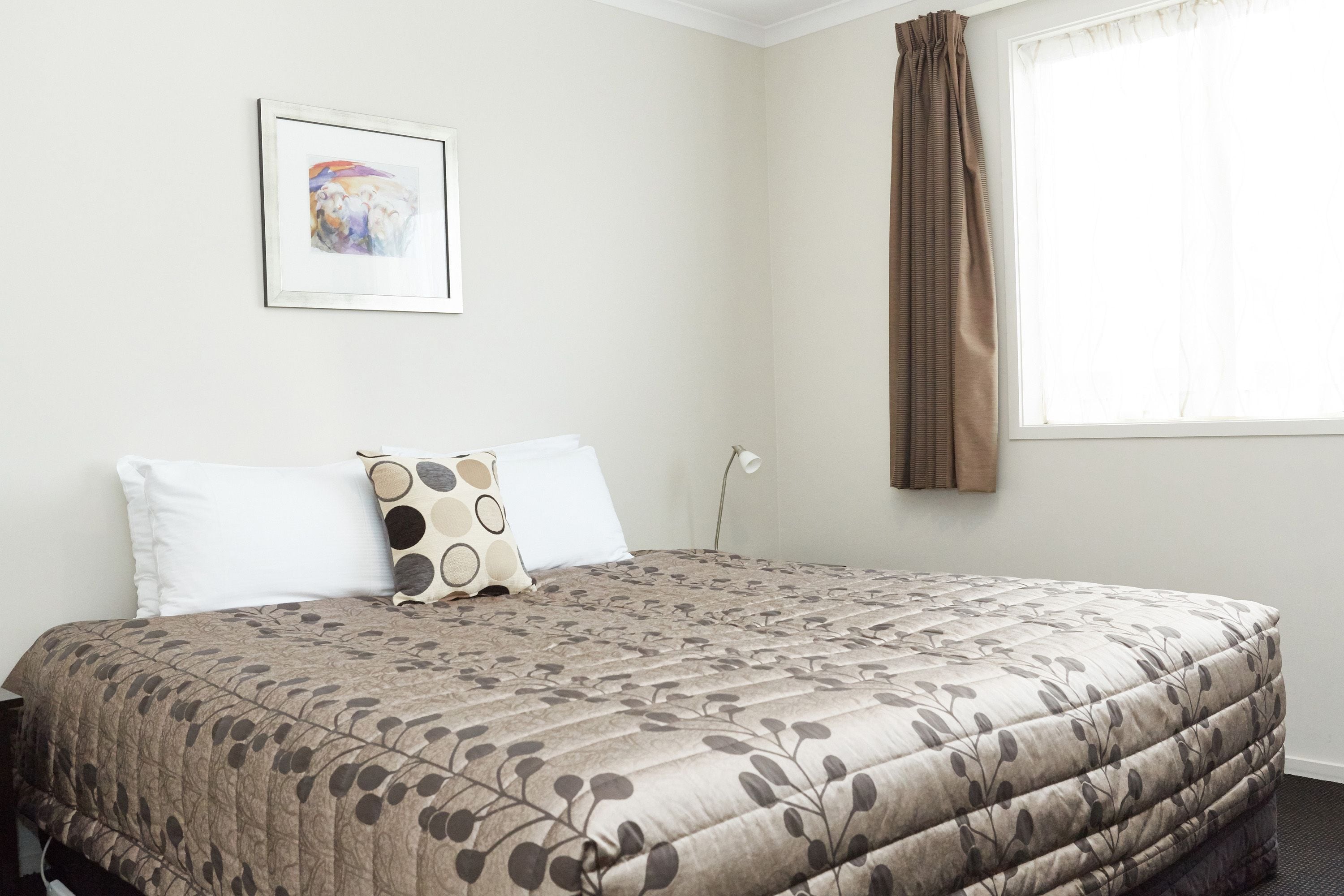A neatly made bed with a floral-patterned bedspread, a single white pillow, and a decorative pillow with circular patterns.