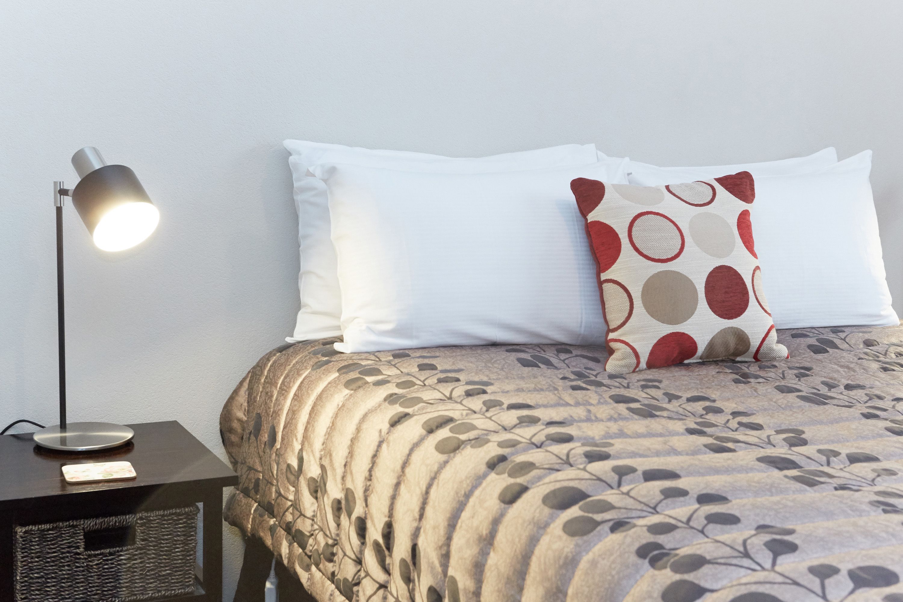 A neatly made bed with a patterned bedspread, a bedside lamp, and a small basket on a nightstand.