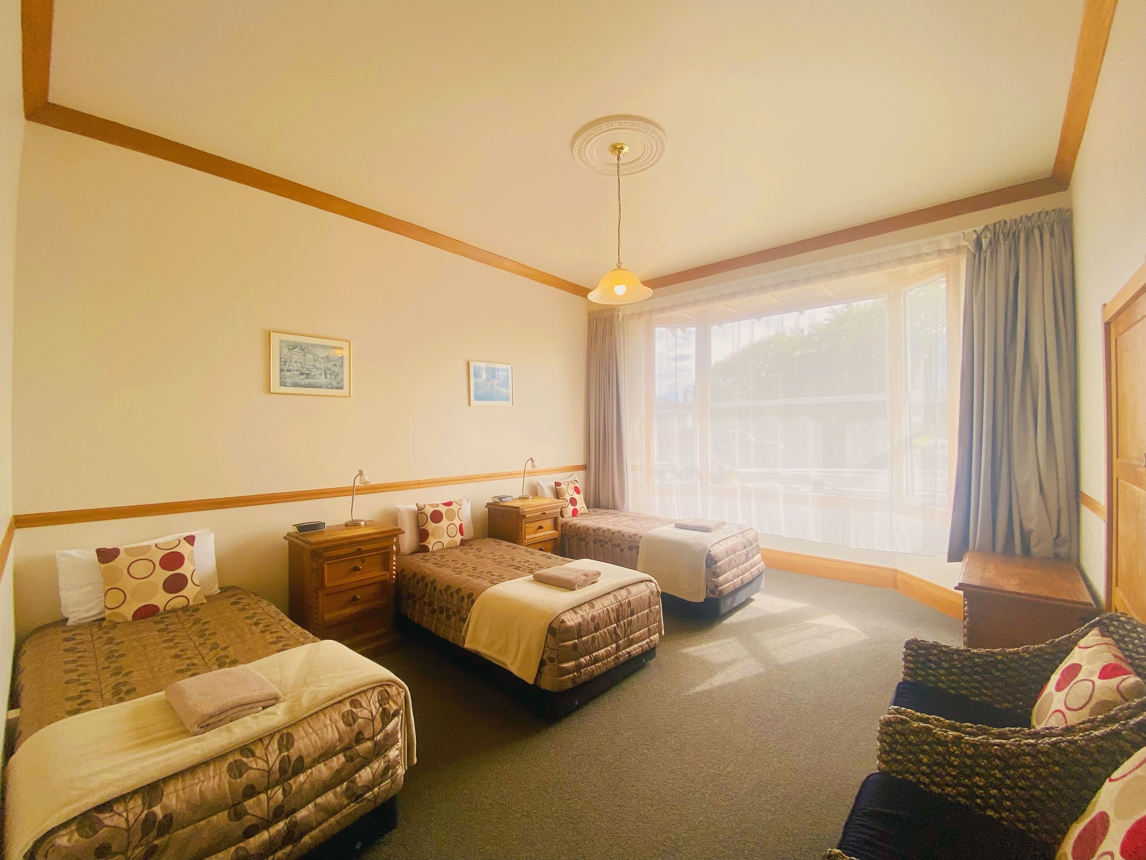 Ein Hotelzimmer mit zwei Betten, einem Fenster mit Vorhängen, einem Deckenventilator und einem kleinen Tisch.